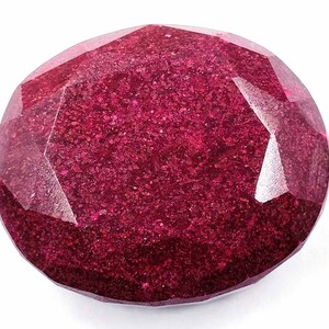 Könnte beinhalten: Ein ovaler Edelstein in tiefem Rot mit einem facettierten Schliff. Der Edelstein hat eine funkelnde, strukturierte Oberfläche.