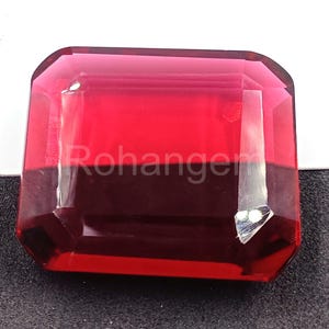 Puede incluir: Una gema roja oscura, tallada en forma rectangular y facetada. La gema tiene una superficie pulida y está colocada sobre un fondo blanco y negro. La palabra "Rohanger" es visible en la superficie de la gema.