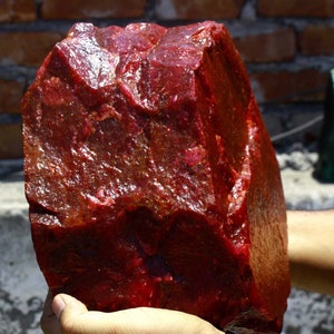 Puede incluir: Una gran gema de rubí rojo sin pulir. El rubí es de color rojo intenso y tiene una superficie brillante y pulida.