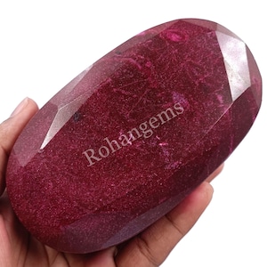 Może przedstawiać: Duży, owalny, ciemnoczerwony kamień szlachetny o błyszczącej, fasetowanej powierzchni. Kamień szlachetny ma lekko metaliczny połysk i jest oznaczony "Rohangems".