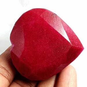 May include: A deep red heart-shaped gemstone with a faceted cut. The gemstone is polished and has a smooth surface.