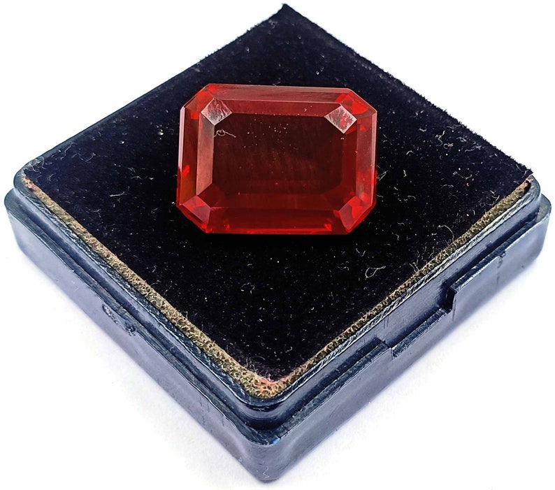 Peut inclure: Une pierre pr&eacute;cieuse rouge de forme rectangulaire, pos&eacute;e dans un &eacute;crin en velours noir.