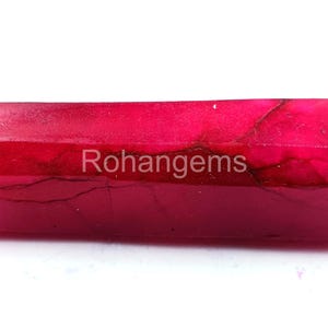 May include: A deep red, faceted, rough ruby gemstone with visible internal lines. Rohangems is printed on the surface of the stone.