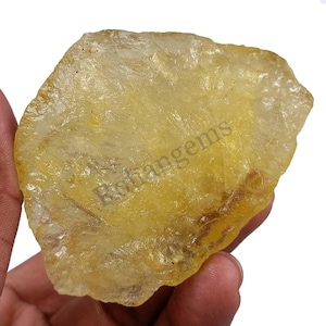 Può includere: Un grande cristallo di citrino giallo grezzo con un aspetto traslucido. Il cristallo ha una forma naturale irregolare ed è tenuto in una mano.