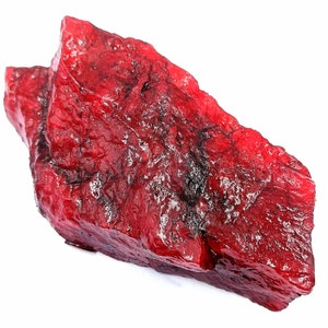 Peut inclure: Une grosse pierre précieuse rouge brute avec une teinte rouge foncé. La pierre précieuse a une surface naturelle non polie.