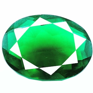 Può includere: Una grande gemma di forma ovale, di colore verde smeraldo, con un design sfaccettato. La gemma ha un motivo a stella con otto punte.