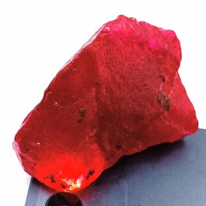 Può includere: Un grande rubino grezzo di colore rosso. Il rubino è traslucido e ha un colore rosso intenso.