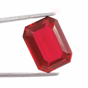 Peut inclure: Une pierre pr&eacute;cieuse rouge fonc&eacute; de taille &eacute;meraude rectangulaire. La pierre pr&eacute;cieuse est tenue par une pince.