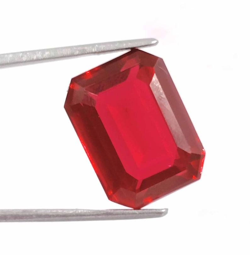 Peut inclure: Une pierre pr&eacute;cieuse rouge fonc&eacute; de taille &eacute;meraude rectangulaire. La pierre pr&eacute;cieuse est tenue par une pince.
