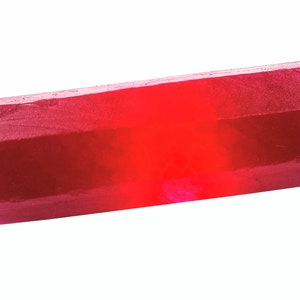 Peut inclure: Un cristal rouge foncé, facetté, allongé avec une surface lisse et polie.