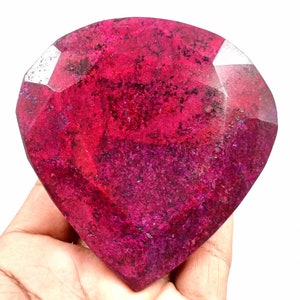 Pode incluir: Uma grande gema de rubi vermelho-escuro com forma de coração facetado. O rubi tem uma aparência ligeiramente nublada com algumas inclusões.