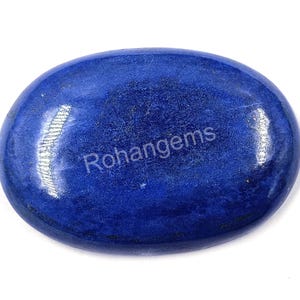 Pode incluir: Gema de lapis-lazúli ovalada e polida. A pedra azul escura tem uma superfície lisa e brilhante com variações sutis de cor e textura. O texto "Rohangems" é visível.