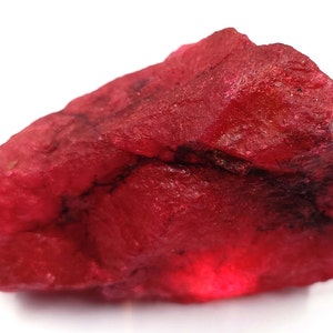 Op de afbeelding: Een grote, ruwe, rode edelsteen met een diepe, rijke kleur. De edelsteen heeft een natuurlijk, onbewerkt oppervlak.