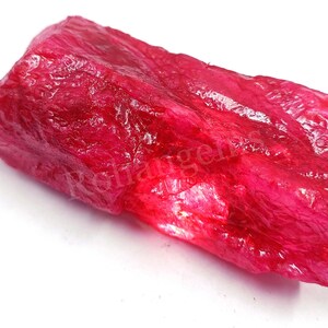 May include: A large, rough, red ruby gemstone. The ruby is a deep, rich red colour and has a natural, unpolished finish.