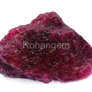 May include: A raw, uncut ruby gemstone in a deep red colour. The surface is textured and uneven, with areas of lighter and darker shades. The image includes the text "Rohangem".