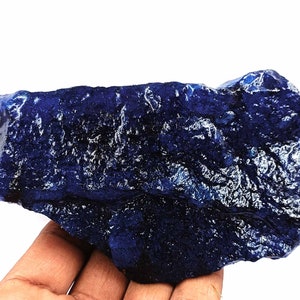 Può includere: Una grande gemma grezza di colore blu scuro. La gemma ha un colore profondo e ricco e una superficie testurizzata.
