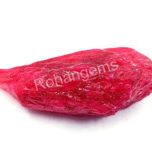 May include: A large, rough, red ruby gemstone. The ruby has a deep, rich red colour and a textured surface.