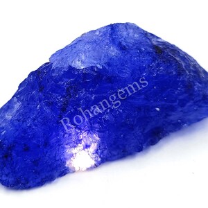 Può includere: Una grande gemma blu grezza con una luce che si riflette su di essa. La gemma è un pezzo grezzo non tagliato di zaffiro blu.