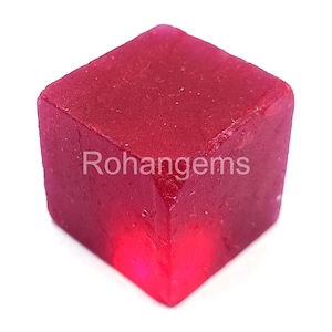 May include: A deep red, square-shaped gemstone with a smooth, polished surface. The gemstone is cut into a cube shape and has a slight shine.