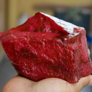 May include: A large, rough, red ruby gemstone. The ruby is a deep, rich red color and has a natural, unpolished finish.