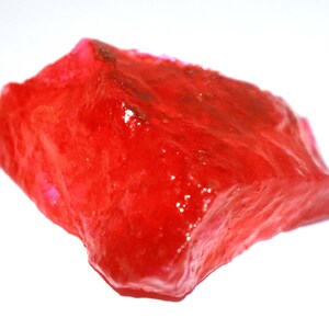May include: A large, rough, red gemstone with a shiny, polished surface.