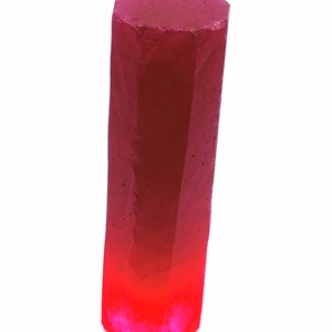 May include: A deep red, faceted gemstone, shaped like a long, hexagonal prism.