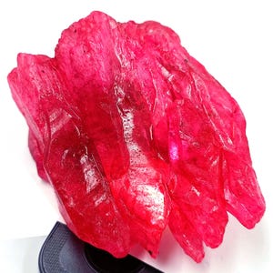 May include: A cluster of deep red ruby crystals with a glassy, translucent appearance. The crystals are sharp and angular, with a rough texture.