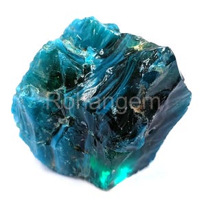 May include: A large, irregularly shaped, teal-colored gemstone with a glossy, reflective surface. The stone has a rough, textured appearance with areas of deep blue and hints of green. The word "Rokangem" is visible on the surface.