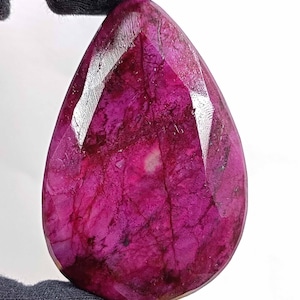 May include: A deep pink gemstone with a faceted pear shape. The gemstone has a natural, organic look with visible inclusions.