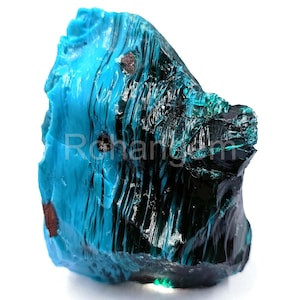 May include: A rough-cut, irregularly shaped gemstone in shades of teal and deep blue. The surface has a glossy, reflective quality, with areas of dark, almost black, coloration. The word "Rehangem" is visible on the surface.