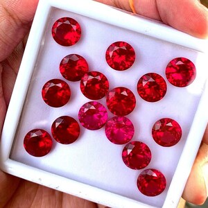 Könnte beinhalten: Eine Sammlung von 14 runden, roten Edelsteinen in einer weißen Schachtel. Die Edelsteine sind in einem Kreis angeordnet.