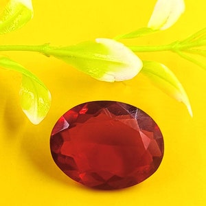 May include: A deep red faceted gemstone with a starburst pattern. The gemstone is on a yellow background.