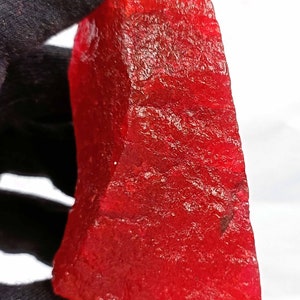 Puede incluir: Una piedra preciosa roja grande y rugosa. La piedra preciosa es de un color rojo intenso y rico y tiene una superficie ligeramente texturizada.
