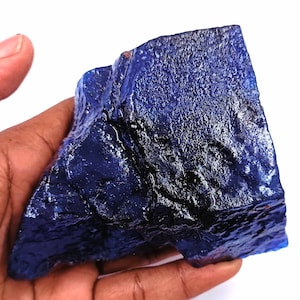 Può includere: Una grande gemma blu scuro, grezza, con una superficie liscia e lucida. La gemma ha un colore profondo e ricco e una forma irregolare.