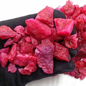 Può includere: Una collezione di pietre preziose di rubino rosa grezzo. I rubini sono di varie dimensioni e forme e hanno un colore rosa intenso e ricco.