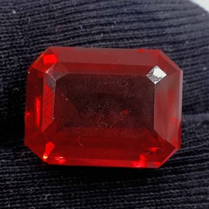 May include: A deep red, emerald-cut gemstone with a high polish.
