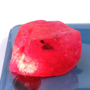 Puede incluir: Una gran gema roja rugosa con una mancha oscura en la superficie.