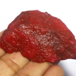 May include: A large, rough, red gemstone with a deep, rich colour. The gemstone has a natural, unpolished finish.