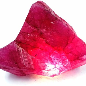 Könnte beinhalten: Ein großer, roher, rosafarbener Rubin-Edelstein. Der Rubin hat eine tiefe, satte Farbe und ist durchscheinend.