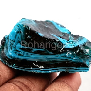 May include: A chunk of layered glass in shades of teal and black. The glass has a marbled appearance with swirling patterns. The word "Rohange" is visible on the surface. The object is held in a hand.