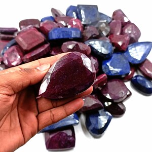 Puede incluir: Un montón de piedras preciosas facetadas sueltas en tonos azul oscuro y rojo burdeos. Las piedras preciosas son de varias formas y tamaños, incluyendo forma de lágrima, ovalada y rectangular.