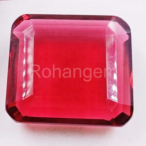 May include: A large, rectangular, faceted gemstone with a deep red hue. The gem has a polished surface and beveled edges. The word "Rohanger" is printed on the surface of the gem. The gem is likely a decorative or collectible item.