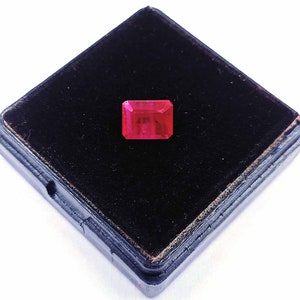 May include: A deep red gemstone with a rectangular shape, set in a black velvet box.