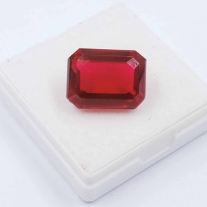 Peut inclure: Une pierre pr&eacute;cieuse rouge fonc&eacute; de taille &eacute;meraude rectangulaire, pr&eacute;sent&eacute;e dans une bo&icirc;te blanche.