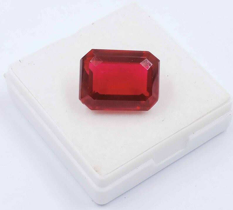 Peut inclure: Une pierre pr&eacute;cieuse rouge fonc&eacute; de taille &eacute;meraude rectangulaire, pr&eacute;sent&eacute;e dans une bo&icirc;te blanche.