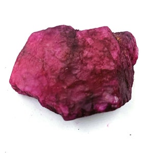 Pode incluir: Um grande cristal de rubi rosa bruto com um tom vermelho intenso. O cristal tem uma aparência natural e não polida.
