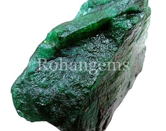May include: A large, rough, green emerald gemstone. The emerald has a deep green color and a rough, natural texture.