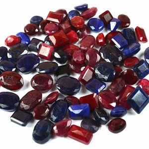 以下が含まれることがあります： 赤いルビーと青いサファイアを含む、ばら売りの宝石のコレクション。宝石はさまざまな形とサイズで、白い背景の上に積み重ねられています。