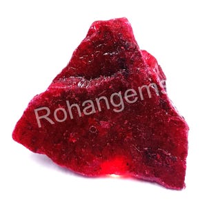 May include: A large, rough, red ruby gemstone. The ruby is a deep red color and has a shiny, glassy surface.