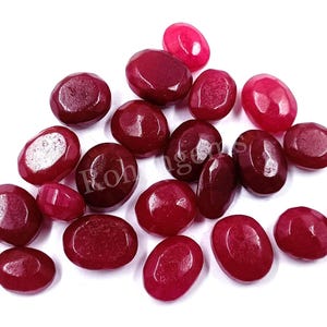 May include: A collection of oval-shaped, faceted, red gemstones. The gemstones are smooth and polished, with a deep red color.